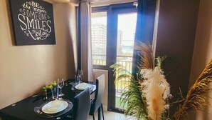 A dining area with a black table set for four, a large window with curtains, and a potted plant with pampas grass. - 1 BR Fully Furnished Condo Across MOA with Pool and Parking - S Res. Unit 0916 (Pasay)