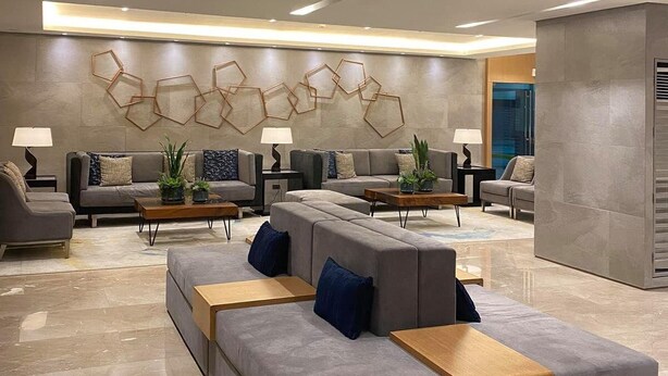 A modern living room with a grey sectional sofa, a coffee table, and a wall with geometric patterns. - 1 BR Fully Furnished Condo Across MOA with Pool and Parking - S Res. Unit 0916 (Pasay)