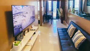 A modern living room with a flat-screen TV, a sofa, and a dining area with a table and chairs. - 1 BR Fully Furnished Condo Across MOA with Pool and Parking - S Res. Unit 0916 (Pasay)