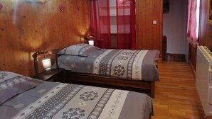 A cozy wooden room with two beds, each with a bedside lamp. A red curtain and a sign that reads "LOVE" are visible.