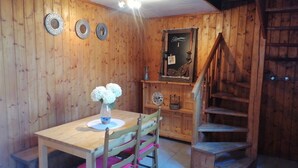 A wooden interior with a dining table, chairs, a vase with flowers, a staircase, and wall decorations.