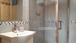 A modern bathroom with a glass-enclosed shower, a white sink with a soap dispenser, and a wooden ceiling.