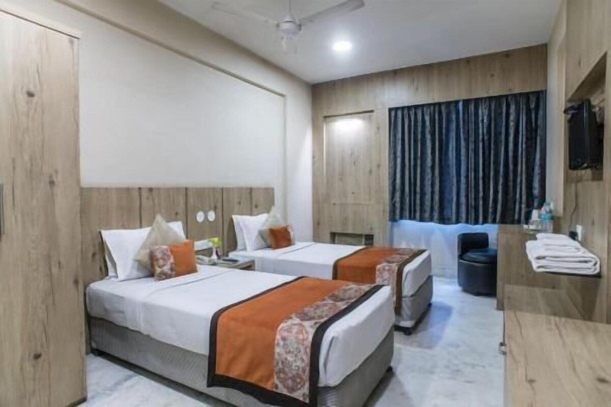 A hotel room with two beds, a wooden headboard, a ceiling fan, a window with curtains, and a small table with a chair.