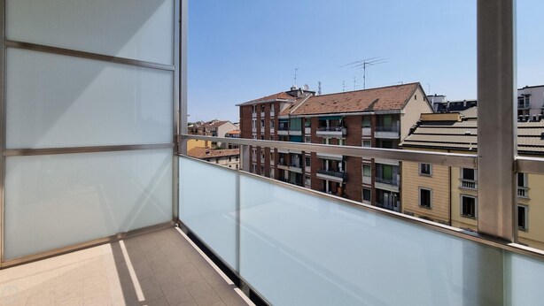 Un balcon offrant une vue dégagée sur les bâtiments adjacents, notamment un immeuble à plusieurs étages doté de balcons et un bâtiment à toit plat.