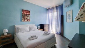 Une chambre à coucher avec un lit, une table de chevet, une lampe, une commode et une fenêtre avec des rideaux.