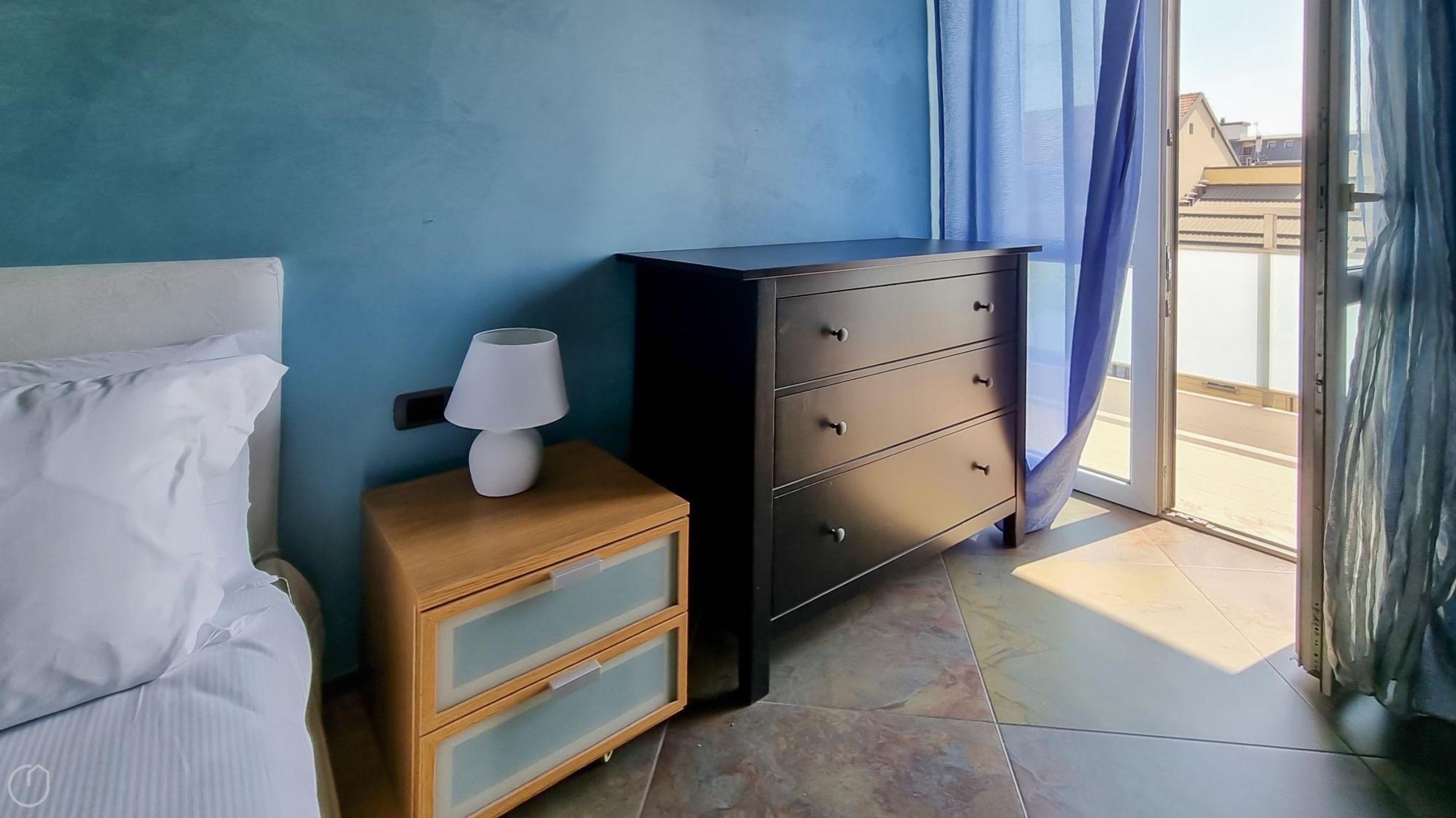 A bedroom with a bed, a nightstand, a dresser, and a window with curtains.