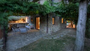 Un bâtiment en pierre doté d’un patio, d’un banc et d’une table avec des coussins.