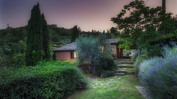 Un jardin avec une maison en briques, des marches en pierre et une végétation luxuriante.