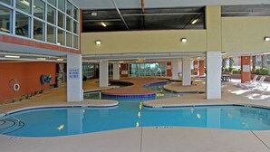 Una piscina interior con señal de agua poco profunda, rodeada por una zona cubierta con asientos y vistas al exterior.