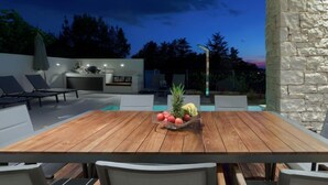 Un espace extérieur aménagé pour les repas, avec une table et des chaises en bois, entouré de murs en pierre et d’une piscine.