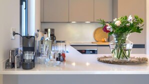 Une cuisine moderne avec un plan de travail blanc, une machine à café et un vase rempli de fleurs.
