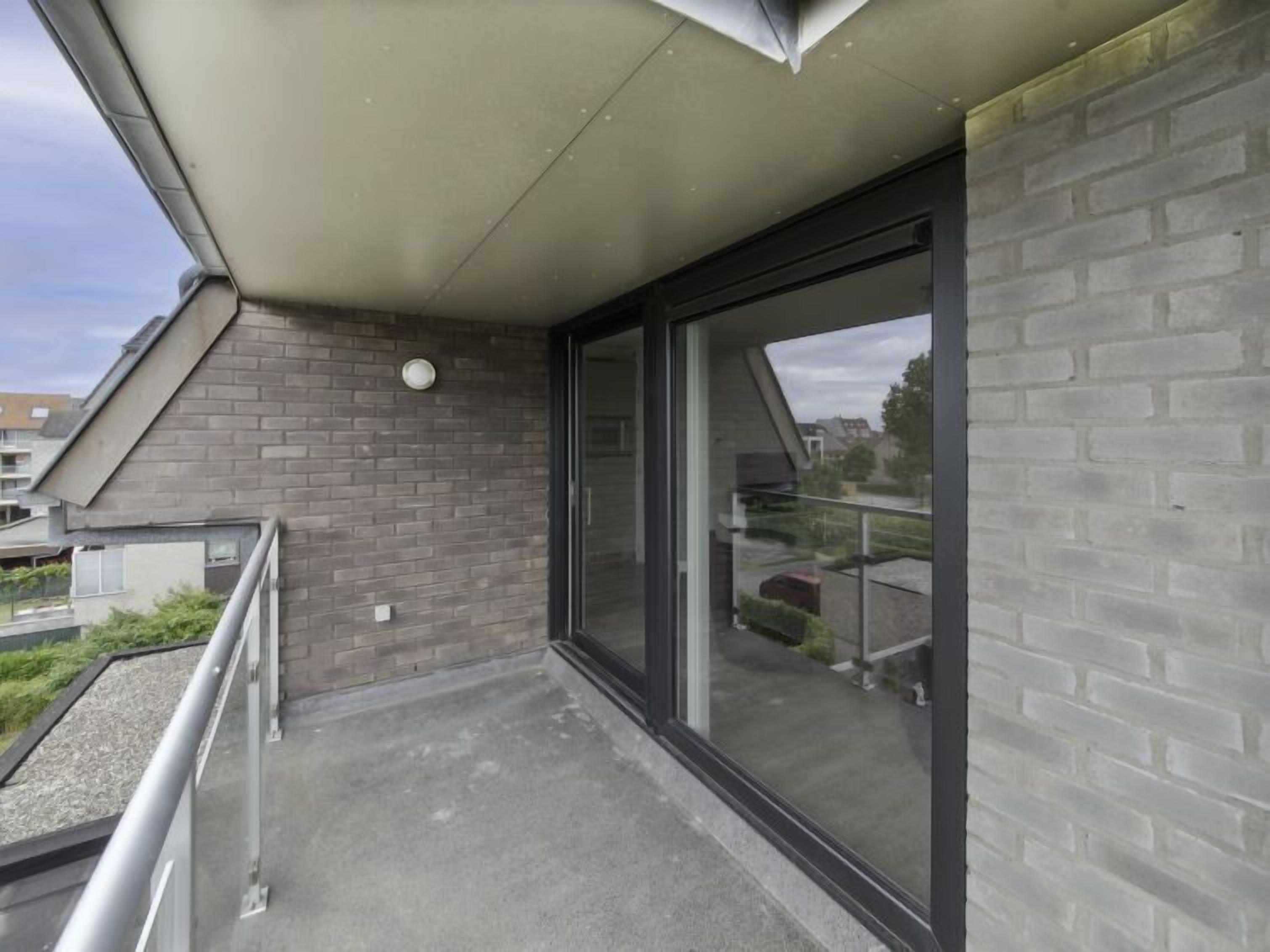 Ein Balkon mit Glastür, Ziegelwand und Metallgeländer.