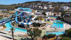 Een waterpark met diverse glijbanen en zwembaden, omgeven door palmbomen en een heuvelachtig landschap op de achtergrond.