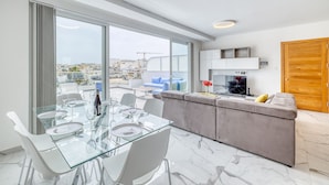 Een moderne woonkamer met een glazen eettafel, een grijze bank en een televisie.