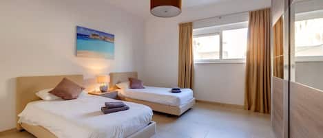 A hotel room with two beds, a painting, a lamp, and a view of the city through large windows.