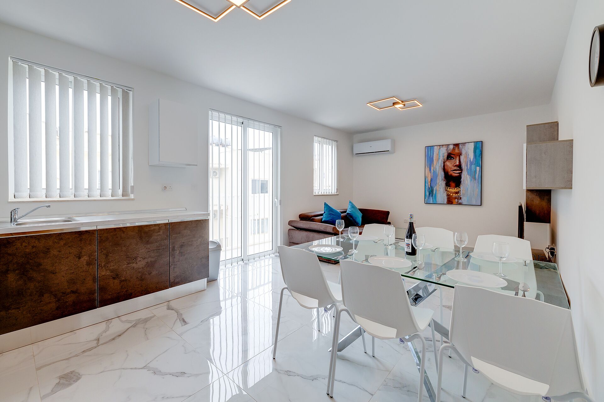 A modern kitchen with a marble countertop and a dining area with a glass table and white chairs.
