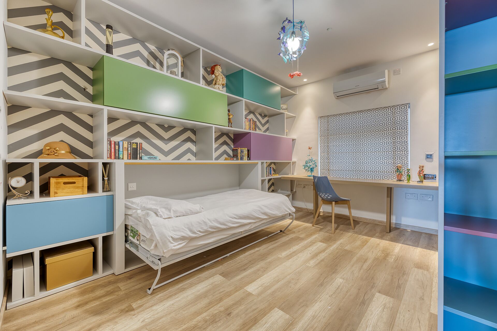 A bedroom with a bed, a desk, and shelves with various items.