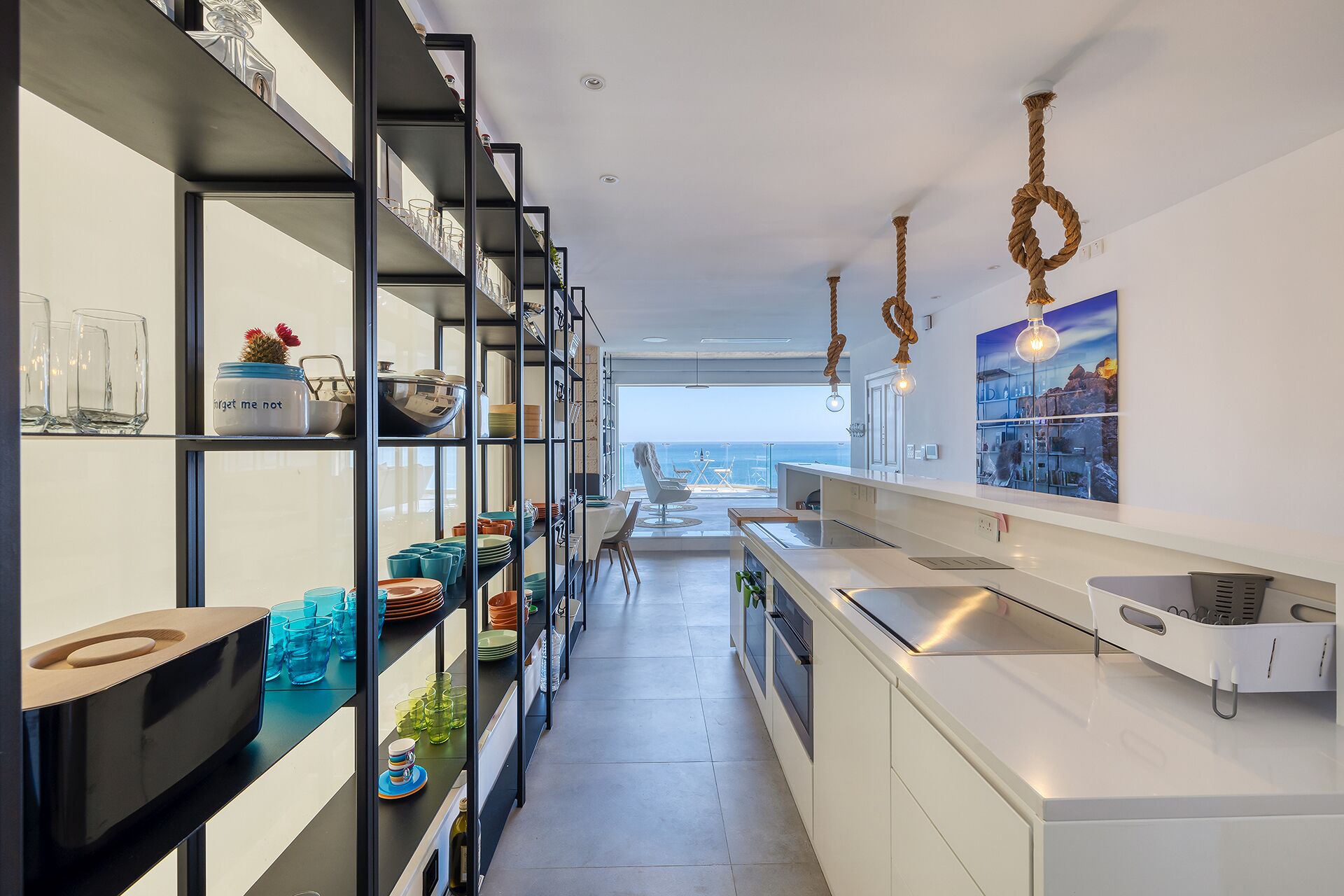 A modern kitchen with open shelving, a view to the sea, and a dining area with a view.