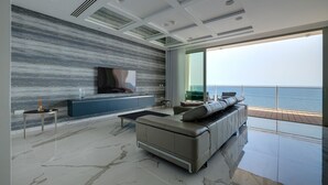 Een moderne woonkamer met een grote televisie, een bank en uitzicht op zee.