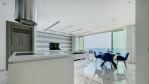Een moderne keuken met een centraal eiland, een eethoek met blauwe stoelen, en een groot raam met uitzicht op zee.