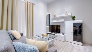 A modern living room with a glass coffee table, a sofa with patterned cushions, a TV, and a white wardrobe.