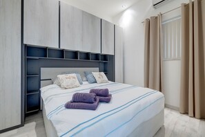 A modern bedroom with a bed, built-in shelving, and a window with curtains.