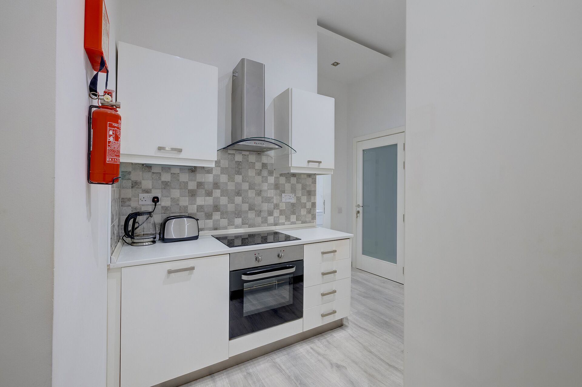 A compact kitchen with white cabinets, a gas stove, a toaster, and a built-in oven.