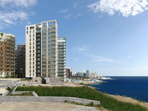 A modern high-rise building with multiple balconies, situated near a coastline. - Luxury Apartment With Pool and Terrace, Top Location (Sliema)