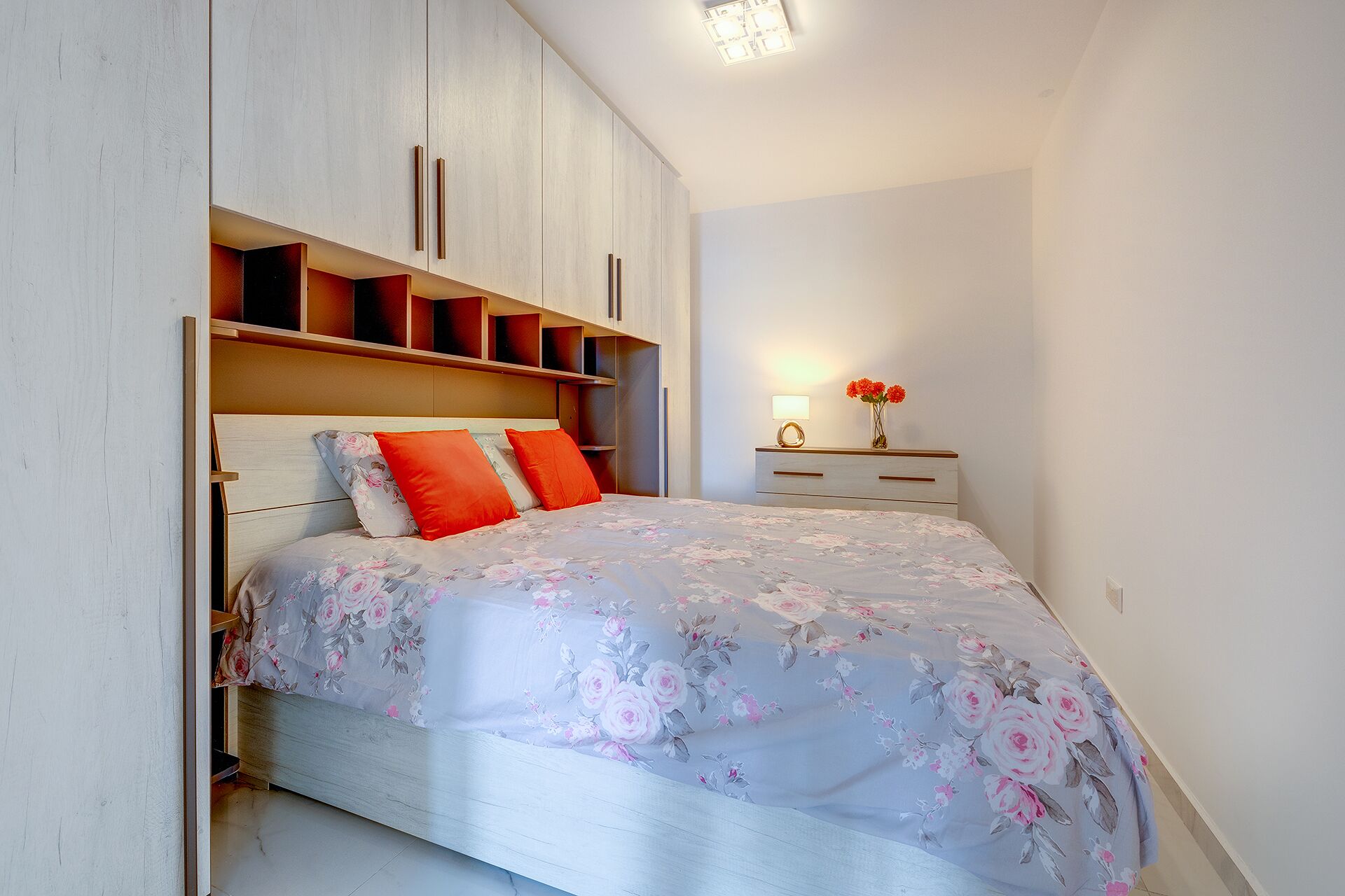 A bedroom with a bed, a nightstand, a lamp, and a shelf unit.
