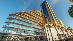 A modern hotel with a curved glass facade, a prominent vertical tower, and palm trees in the foreground. - Splendid 2BR Apartment, Steps to St Georges Bay (Swieqi)