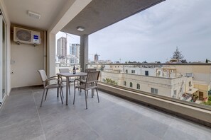 A balcony with a table and chairs, overlooking a cityscape with buildings and construction cranes.
