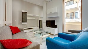 A modern living room with a glass coffee table, a flat-screen TV, and a sofa with red cushions. - Modern Apartment in the Best Area of Sliema (Sliema)