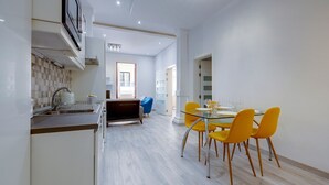A modern kitchen with a built-in dishwasher, a dining area with a glass table and yellow chairs, and a view of a balcony. - Modern Apartment in the Best Area of Sliema (Sliema)