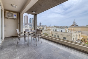 A balcony with a table and chairs, overlooking a cityscape with buildings and construction cranes.