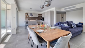 Een moderne keuken met een centraal eiland, een eetgedeelte met een houten tafel, en een woonkamer met een blauwe bank.