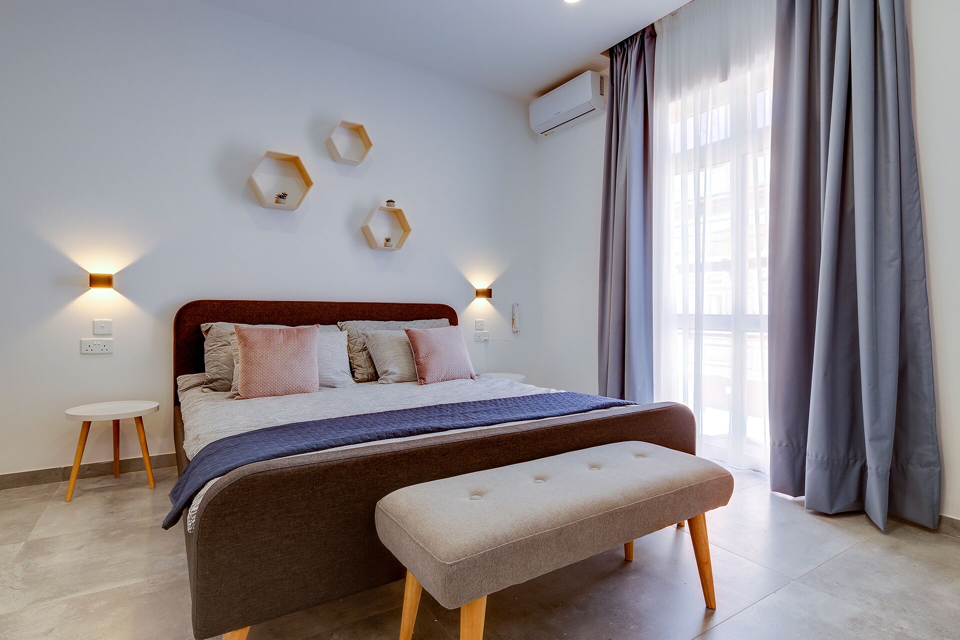 Ein modernes Schlafzimmer mit Bett, Nachttischen, einer Bank und dekorativen Wandleuchten.