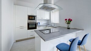A modern kitchen with white cabinets, a built-in oven, a glass island with bar stools, and a vase with flowers. - Spacious Apartment Steps to the Promenade (Gzira)