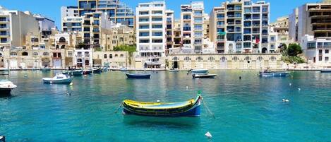 A marina with several boats docked, surrounded by multi-story buildings with balconies and windows.