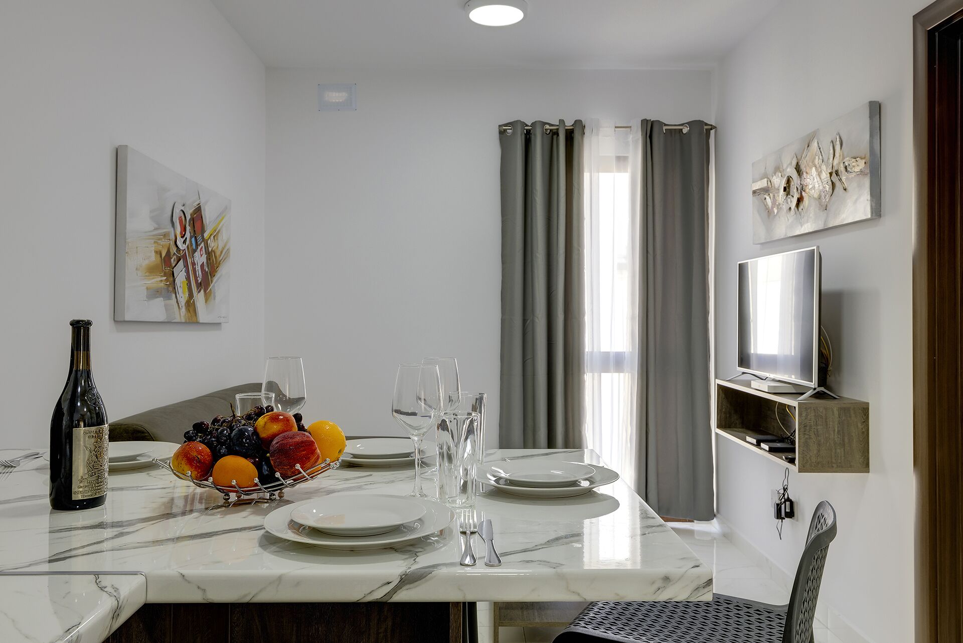 A dining area with a marble table, fruit bowl, wine bottle, and glasses.