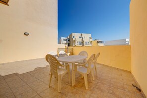 A small outdoor patio with a table and chairs, a tiled floor, and a view of white buildings in the background. - Modern 2 Bedroom Maisonette in Central Sliema (Gzira)