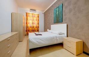 A bedroom with a bed, a wardrobe, a nightstand, and a painting on the wall. - Modern 2 Bedroom Maisonette in Central Sliema (Gzira)