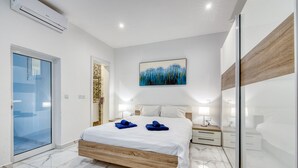 A modern bedroom with a large bed, a glass shower enclosure, a painting above the bed, and a wooden accent wall. - Modern 1BR Apartment, Central Location (Gzira)