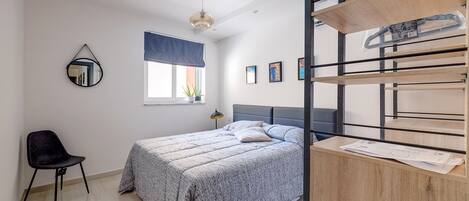 Un dormitorio con cama, una silla, un ventanal con vistas y un escritorio con documentos.
