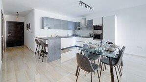 A modern kitchen with a central island, built-in appliances, and a dining area with a glass table and chairs. - Chic 2BR Apartment, Ideal Location (Ta' Xbiex)
