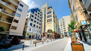 A modern urban street with multi-story buildings, a central plaza with benches, and a clear sky. - Chic 2BR Apartment, Ideal Location (Ta' Xbiex)