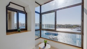 Een kamer met grote ramen met uitzicht op een waterkant, een tafeltje met een plant en een spiegel aan de muur.