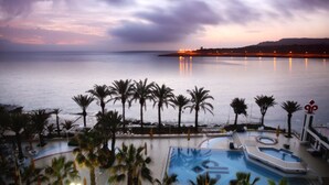 Un complexe hôtelier doté d’une piscine, de palmiers et offrant une vue sur la mer au coucher du soleil.