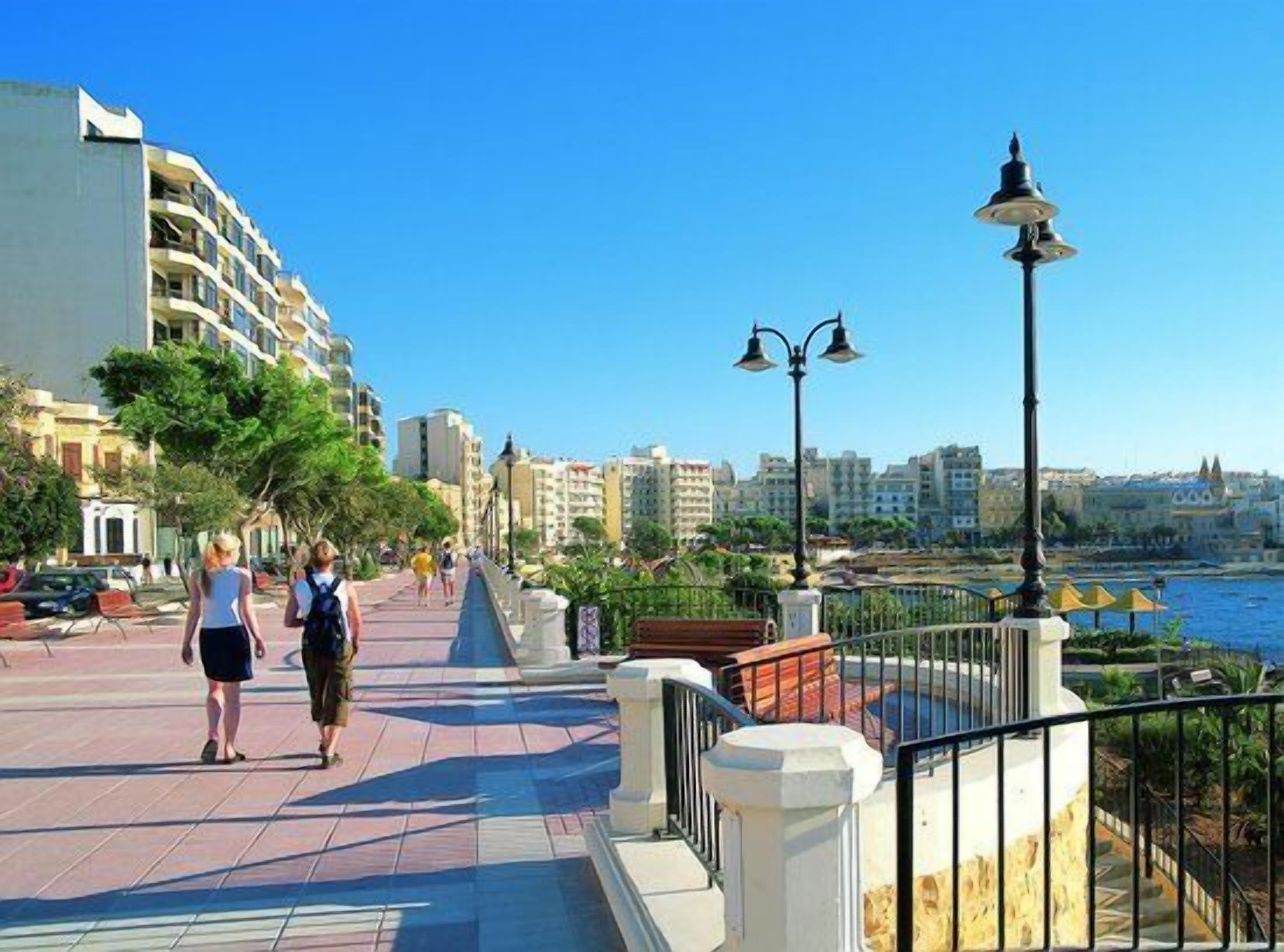 A waterfront promenade with a paved walkway, benches, and street lamps.
