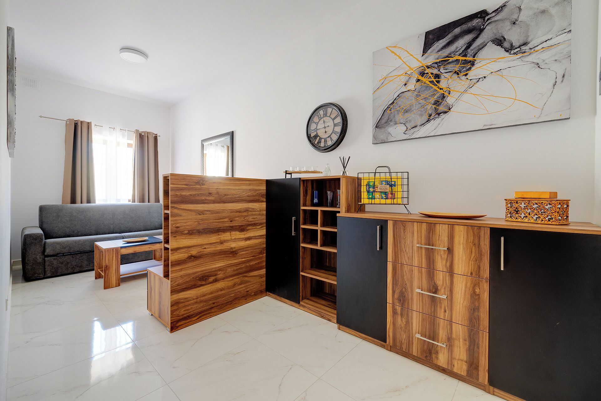 Eine moderne Küche mit Holzschränken, einem schwarzen Kühlschrank und einer Essecke mit einem grauen Sofa.