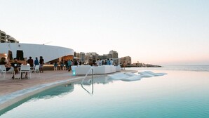 An infinity pool with lounge chairs and a seating area, overlooking the sea with buildings in the background. - Duplex Luxury Apartment in Portomaso With Pool (St. Julian's)